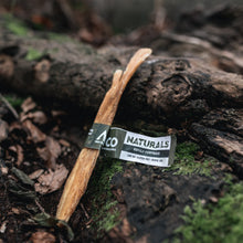 Load image into Gallery viewer, Two wooden sticks tied together with a label on a forest floor.