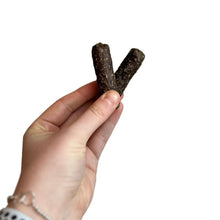 Load image into Gallery viewer, Hand holding two dark brown dog treats against a white background