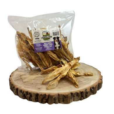 A clear plastic package containing air-dried rabbit ears for dogs, with a wooden slice in the background.