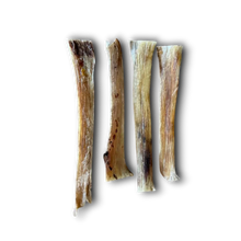 Load image into Gallery viewer, Four natural dog bones, varying in size and showing natural tan, brown, and cream colors, arranged vertically on a plain white background.
