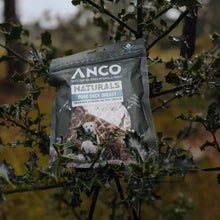Load image into Gallery viewer, A bag of Anco Naturals Pure Duck Breast dog food hanging from a leafy green branch in an outdoor, natural setting.

