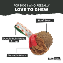 Load image into Gallery viewer, A Barks Super Chewer dog toy with a brown textured ball, red plush tearable section, and striped fabric strap, shown on a white background with text callouts reading 'Double Reinforced Strap,' 'Tearable Plush,' and 'Beef Scent.'.

