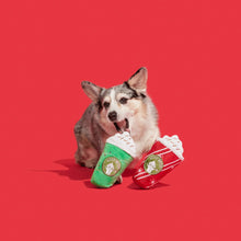 Load image into Gallery viewer, A corgi dog holds a plush popcorn-shaped toy in its mouth against a solid red background. The toy is designed to look like a hot dog in a popcorn bun, with one half in green and the other in red with white stripes and a gold circular logo.
