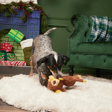 Load image into Gallery viewer, A black, white, and tan dog plays with a brown plush toy on a white shag rug in a decorated holiday living room with a green sofa and fireplace.
