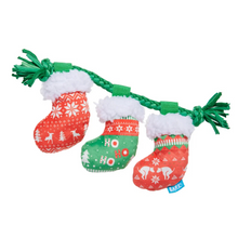 Load image into Gallery viewer, A three-motley Christmas stocking dog toy on a white background. The toy features three festive knit stockings in red, green, and orange with white patterns, attached to a green braided rope with white faux fur trim and green tassel ends.
