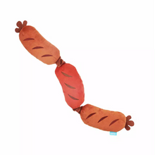 Load image into Gallery viewer, A plush dog toy shaped like three linked sausages, with alternating light brown and reddish-brown sections, dark brown grill marks, and a small blue tag near one end, shown on a plain white background.
