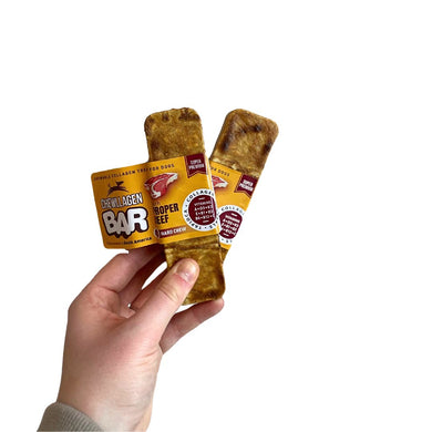 A hand holding two Chewllagen Beef Bar treats, which are dog treats made from collagen, shaped like a bar, with visible texture and a golden-brown color.