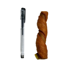 Load image into Gallery viewer, A clear pen with a black clip and tip placed next to a twisted, golden-brown pastry or pretzel-like snack on a white speckled surface.
