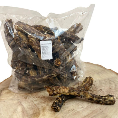 Packaged duck necks for dogs placed on a wooden surface, with some duck necks scattered in front.