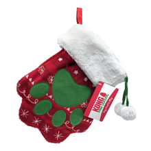 Load image into Gallery viewer, A red and white plush dog stocking with a paw shape, hanging by a green ribbon, with dangling pom-poms and a KONG logo tag.
