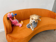 Load image into Gallery viewer, A golden retriever dog lies on a curved orange velvet sofa, chewing on a gray plush toy. A pink flamingo plush toy and a small hammer plush are also on the sofa against a plain indoor wall.

