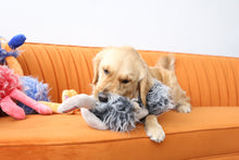 Load image into Gallery viewer, A golden retriever dog is lying on an orange sofa, chewing on a gray plush stuffed animal. Other colorful plush toys are partially visible on the left side of the sofa.
