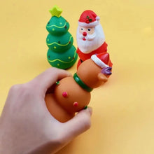 Load image into Gallery viewer, A hand is squeezing a brown reindeer toy with a green collar and purple horn, with two Christmas-themed toys behind it on a yellow background: a green Christmas tree and a Santa Claus figure.
