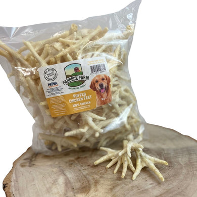 A package of Nova Paddock Farm Puffed Chicken Feet 1kg, displayed on a wooden surface with a happy dog depicted on the label.